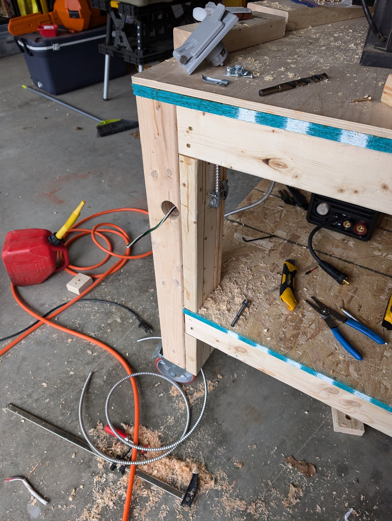 Workbench leg detail showing a cable opening, metal conduit, and shelf support